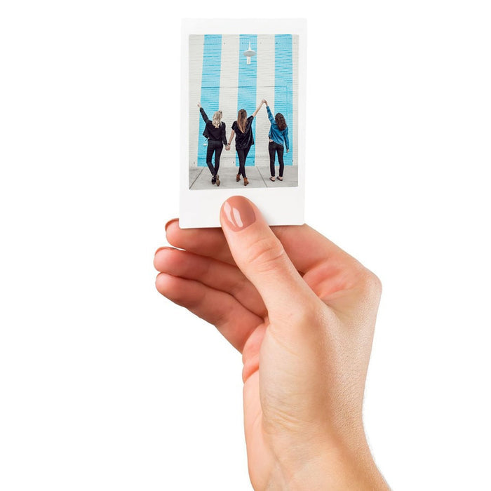 Hand holding a small photo print of three people against a blue wall.