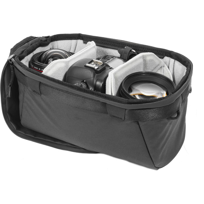 Black handheld Peak Design Camera Cube V2 with adjustable dividers, zipper closure, and durable nylon exterior, perfect for carrying camera gear safely.