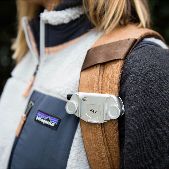 The Silver version of the Peak Design Capture Camera Clip V3 attached to a backpack strap.