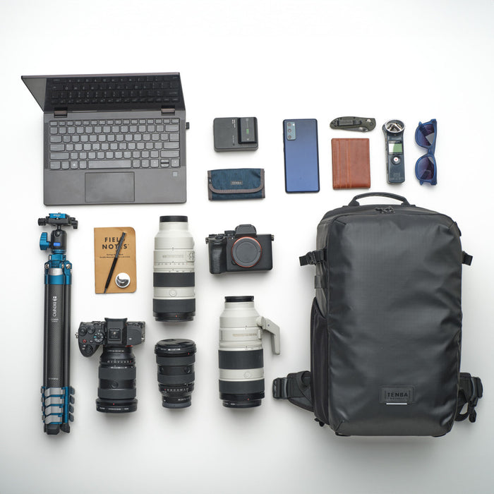 Collection of travel or photography equipment including a laptop, backpack, camera, lenses, and other accessories on a white background.